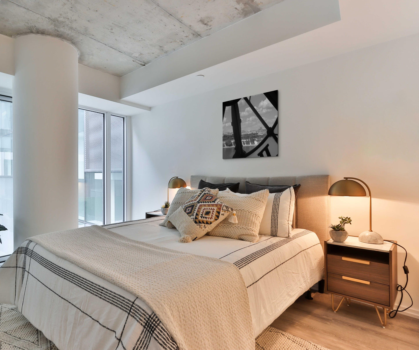 French Clock Canvas Wall Art in loft bedroom with white walls, white and black quilt, brown side table and brown lamp