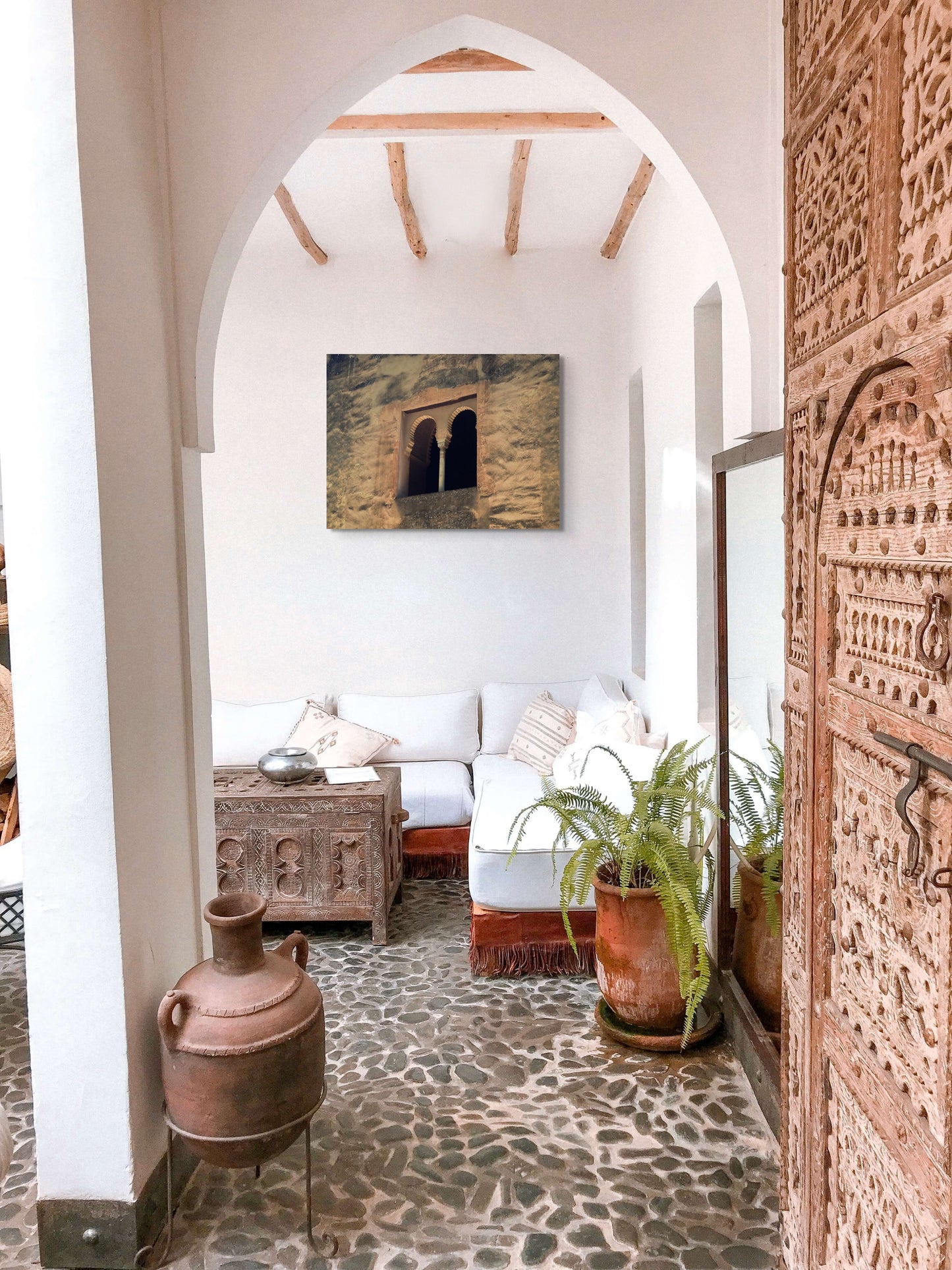 Palace Window Canvas Wall Art in outdoor balcony with white walls and arched doorway, white lounge, rustic urn, stone flooring and wooden coffee table