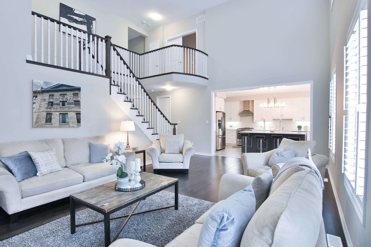 Old Warehouse Canvas Wall Art in lounge room with white walls, cream lounge, staircase, kitchen with island, pale blue cushions, square rug and dark wooden floorboards