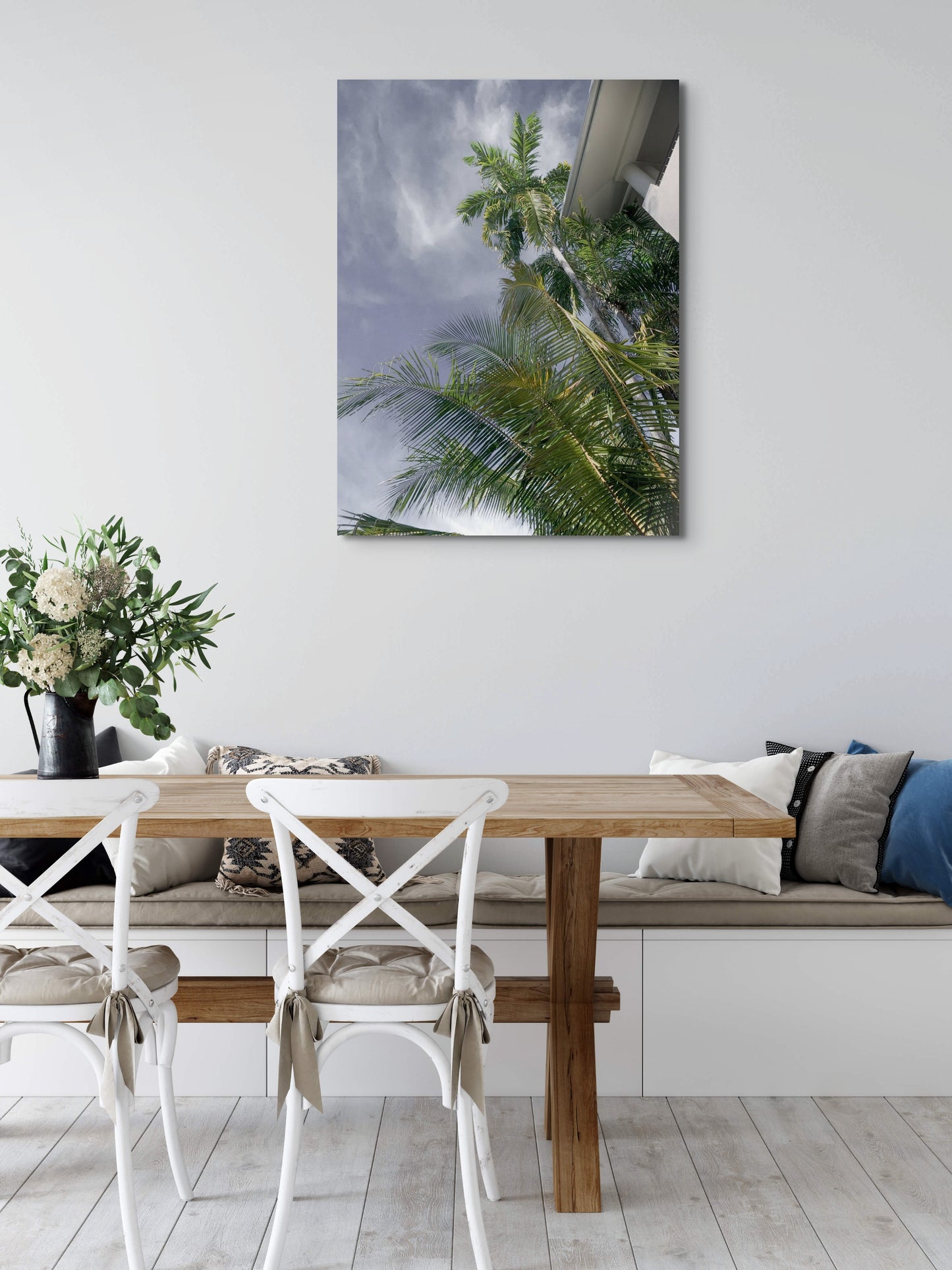 Palm Tree Dreaming Canvas Wall Art in kitchen with white wall, long bench seat with various cushions, wooden dining table and two white chairs